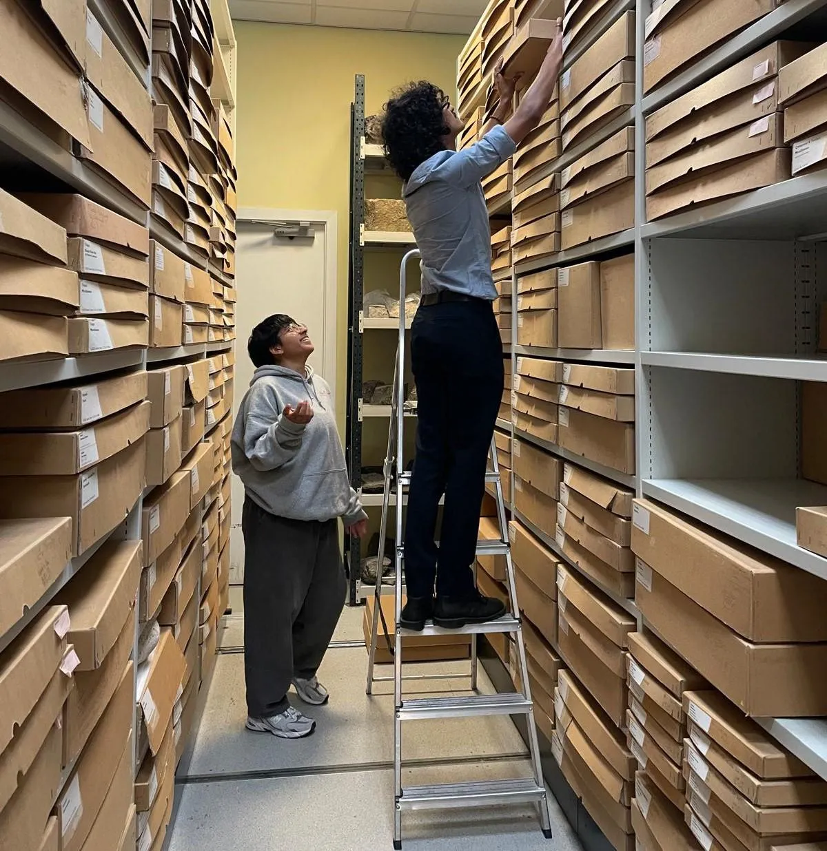 Two students in the Museum stores retrieve a box from the shelves of material.