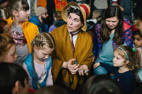 Children surround a performer dressed as Mary Anning.