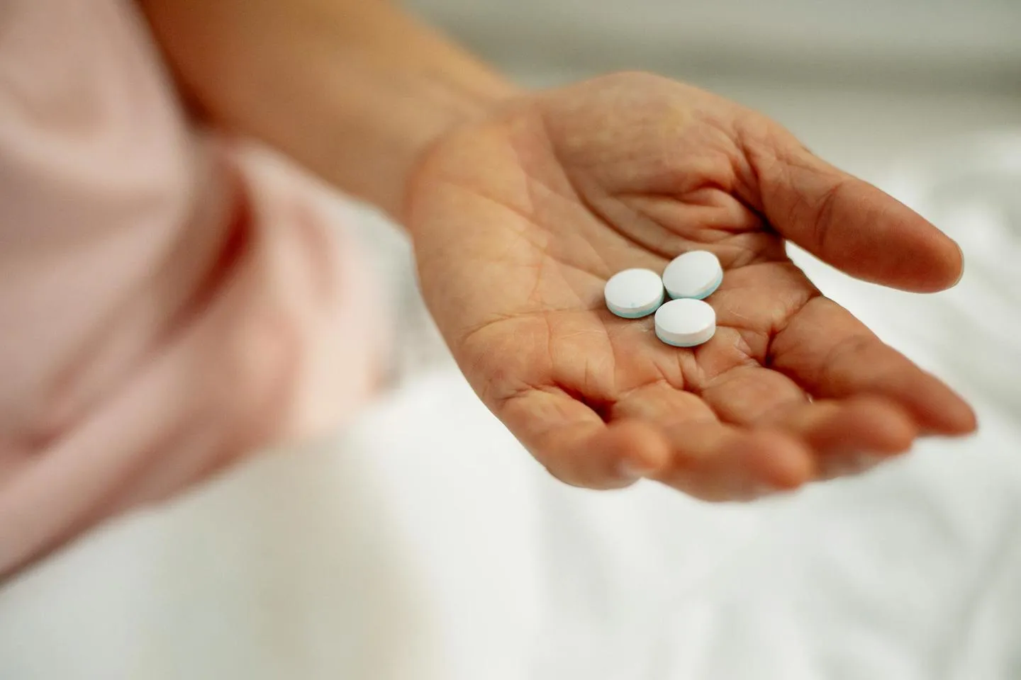 A close-up of three white pills in the palm of a woman's hand