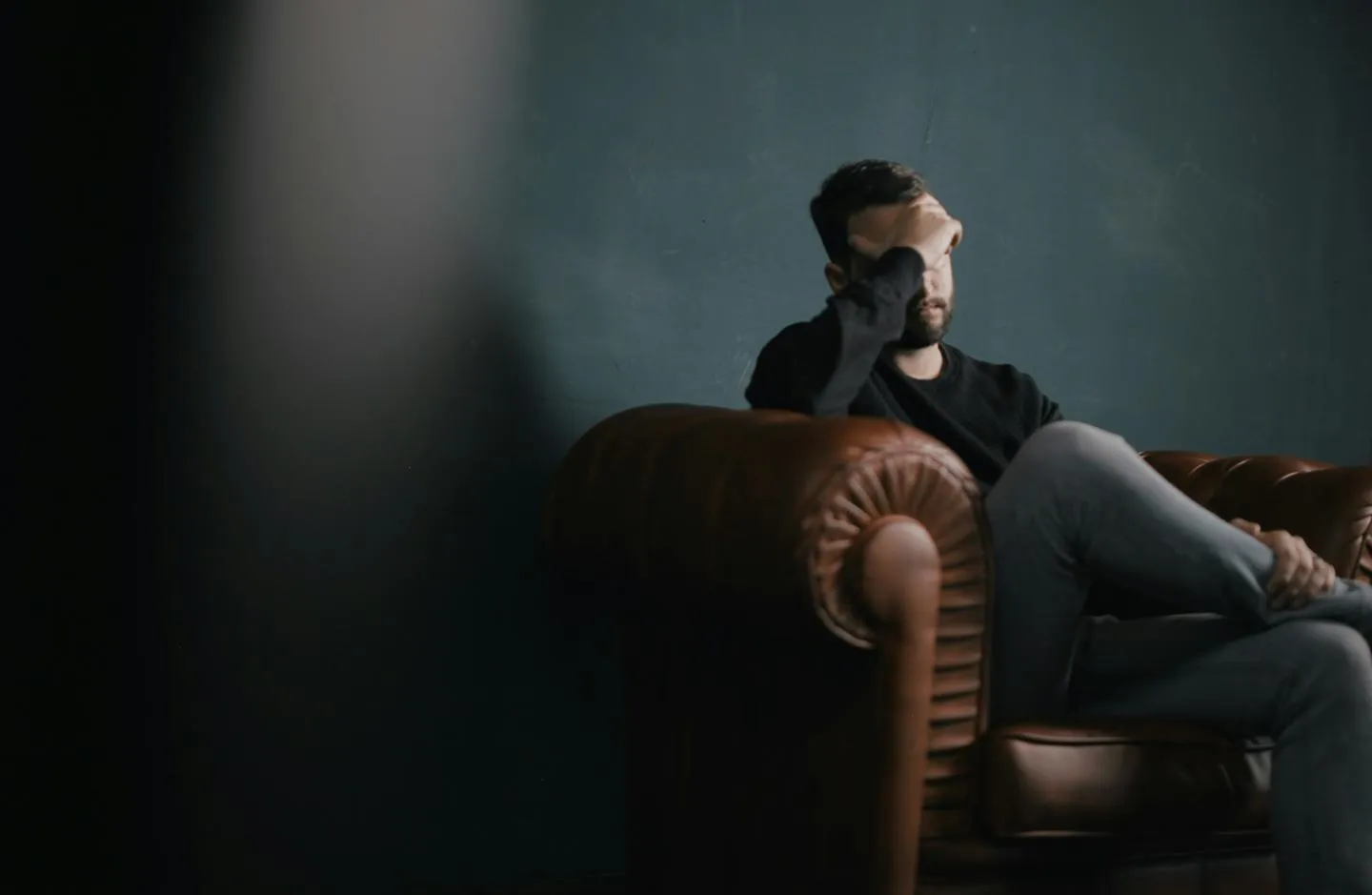 A troubled-looking man sitting on a sofa with his head in hands