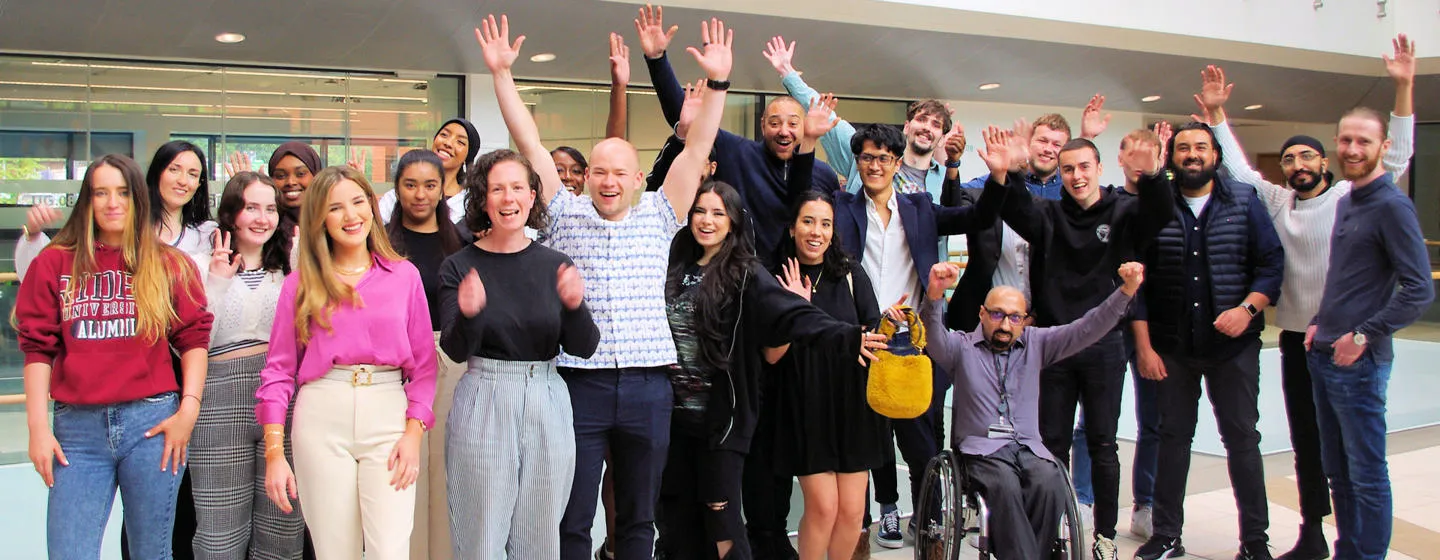 A group of UoB students smiling and holding their hands in the air in celebration