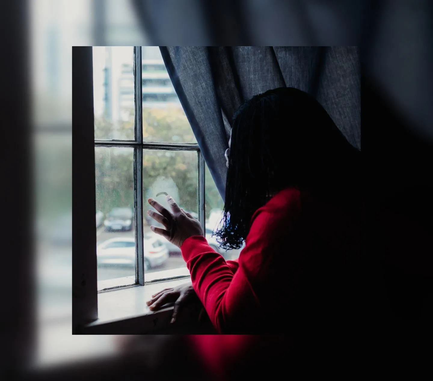 Woman with dark hair and red top staring through a window
