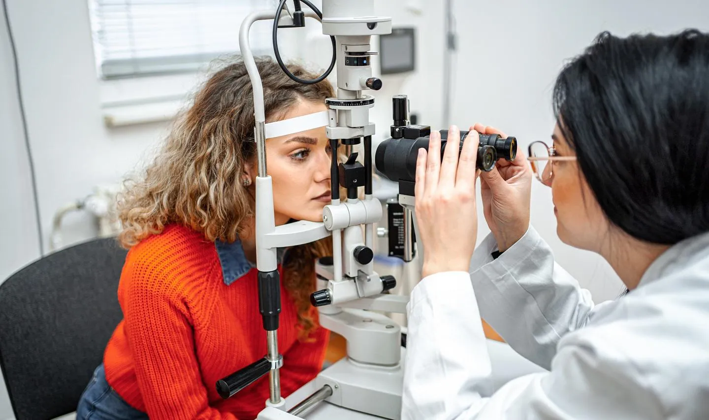 Ophthalmologist performing eye exam with optical equipment on female patient