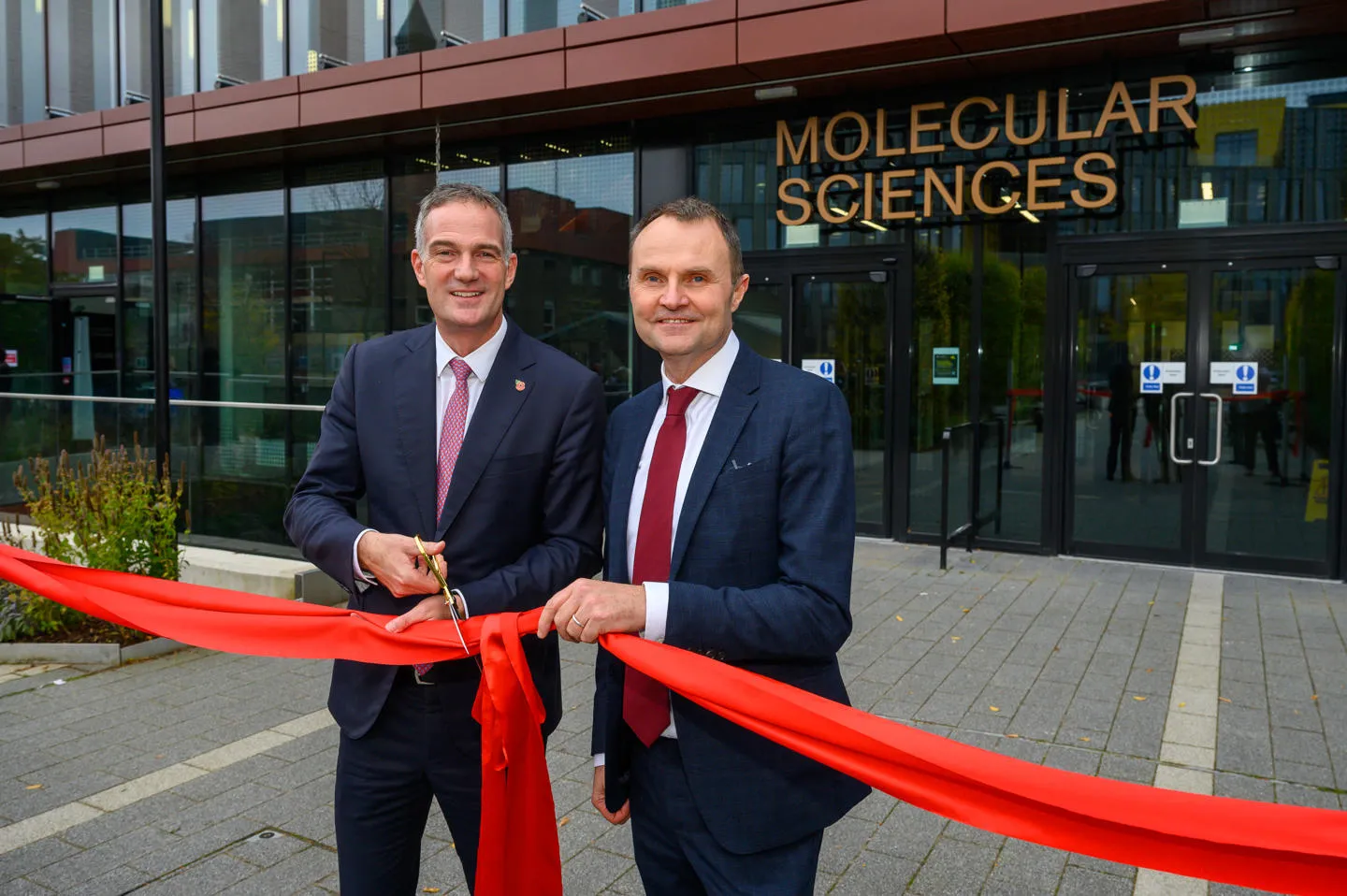 Rt Hon Peter Kyle MP with Professor Adam Tickell cutting red ribbon in front of Molecular Sciences Building