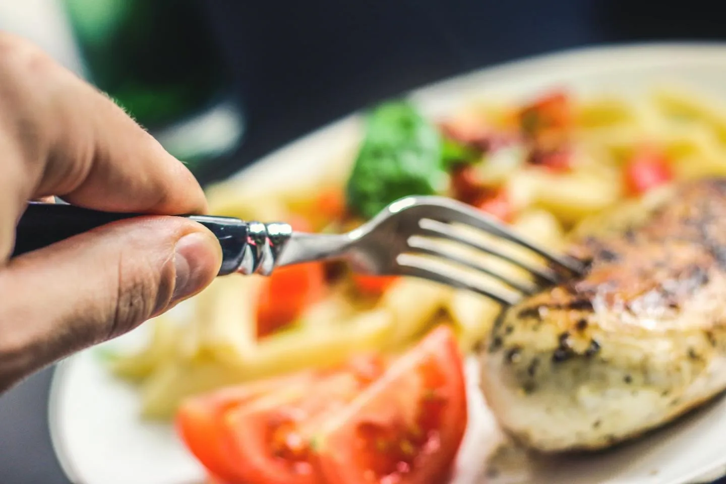 Food such as chicken and tomatoes on a plate with someone holding a fork.