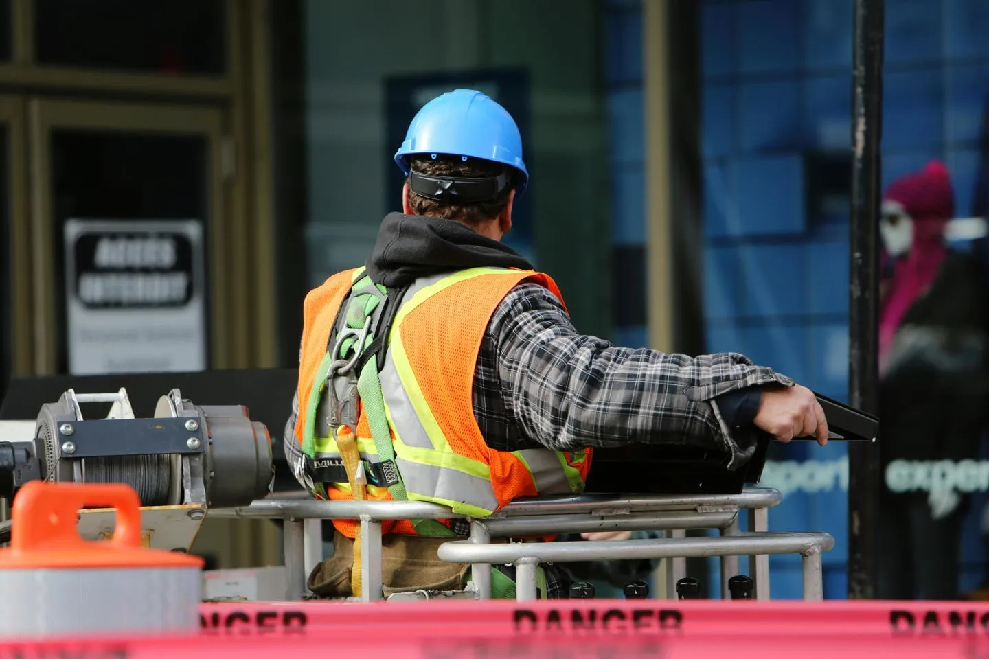 Construction worker with a hard hat behind danger tape, on a construction site.