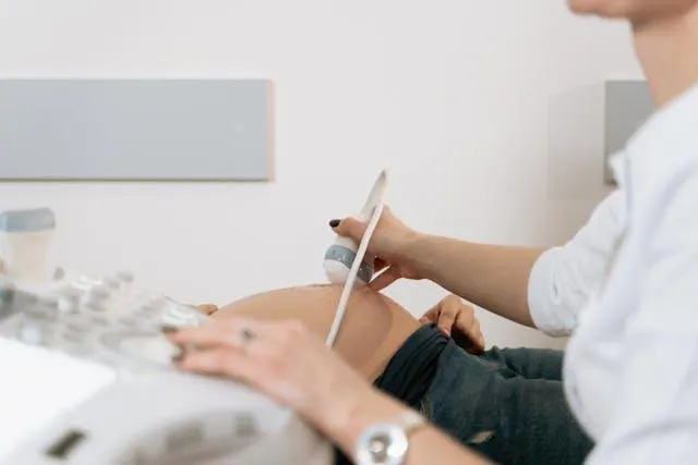 A doctor in the foreground doing a pregnant woman's ultrasound scan.