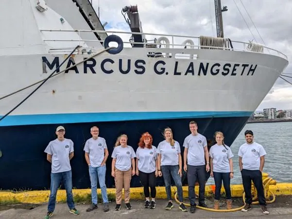 eight people stood in front of a large ship with MARCUS G.LANGSETH written on the side of it.