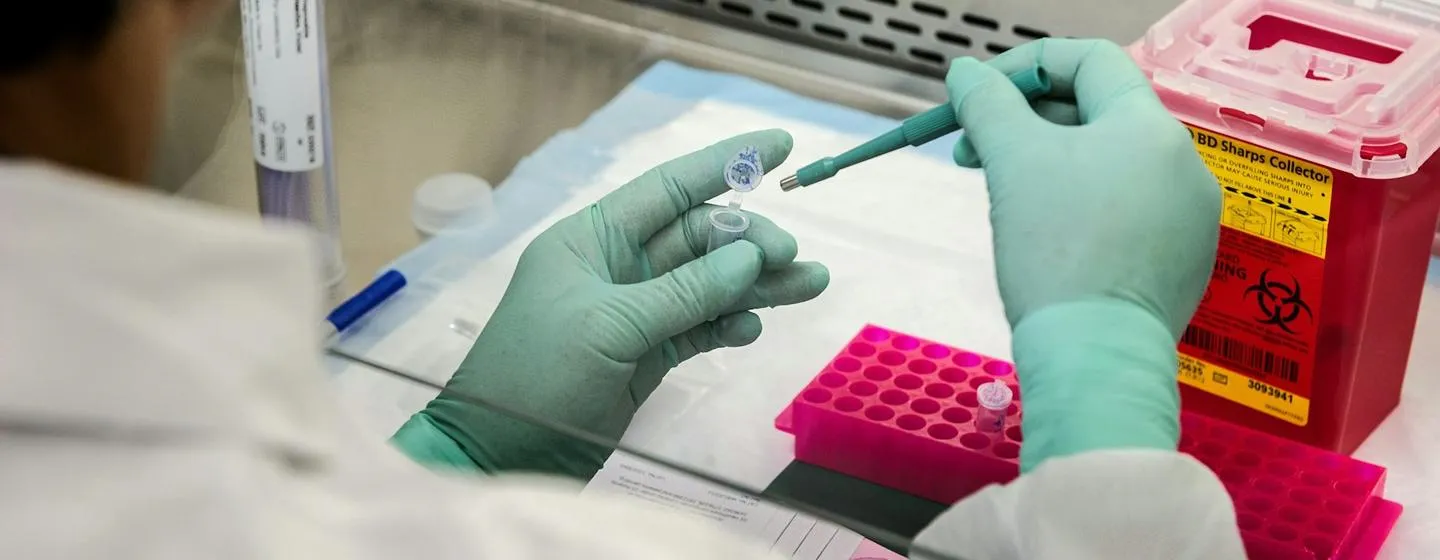 Gloved hands transferring liquid to a vial with a pipette