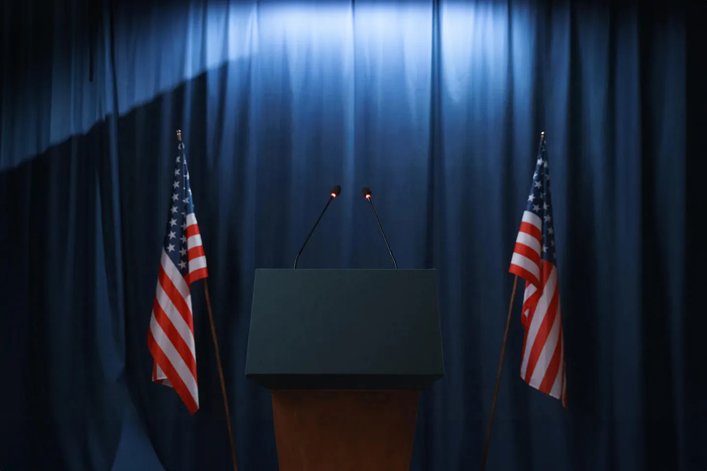 A debate plinth with microphones standing next to two American flags.