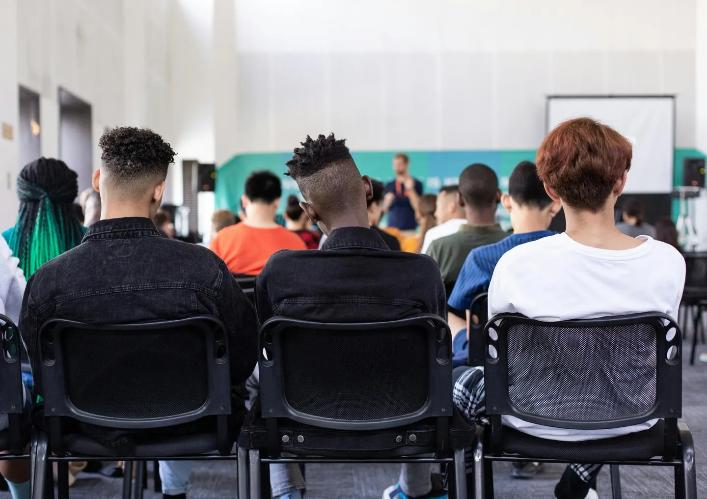 The backs of three teenage boys' heads as they listen to a talk in a large classroom