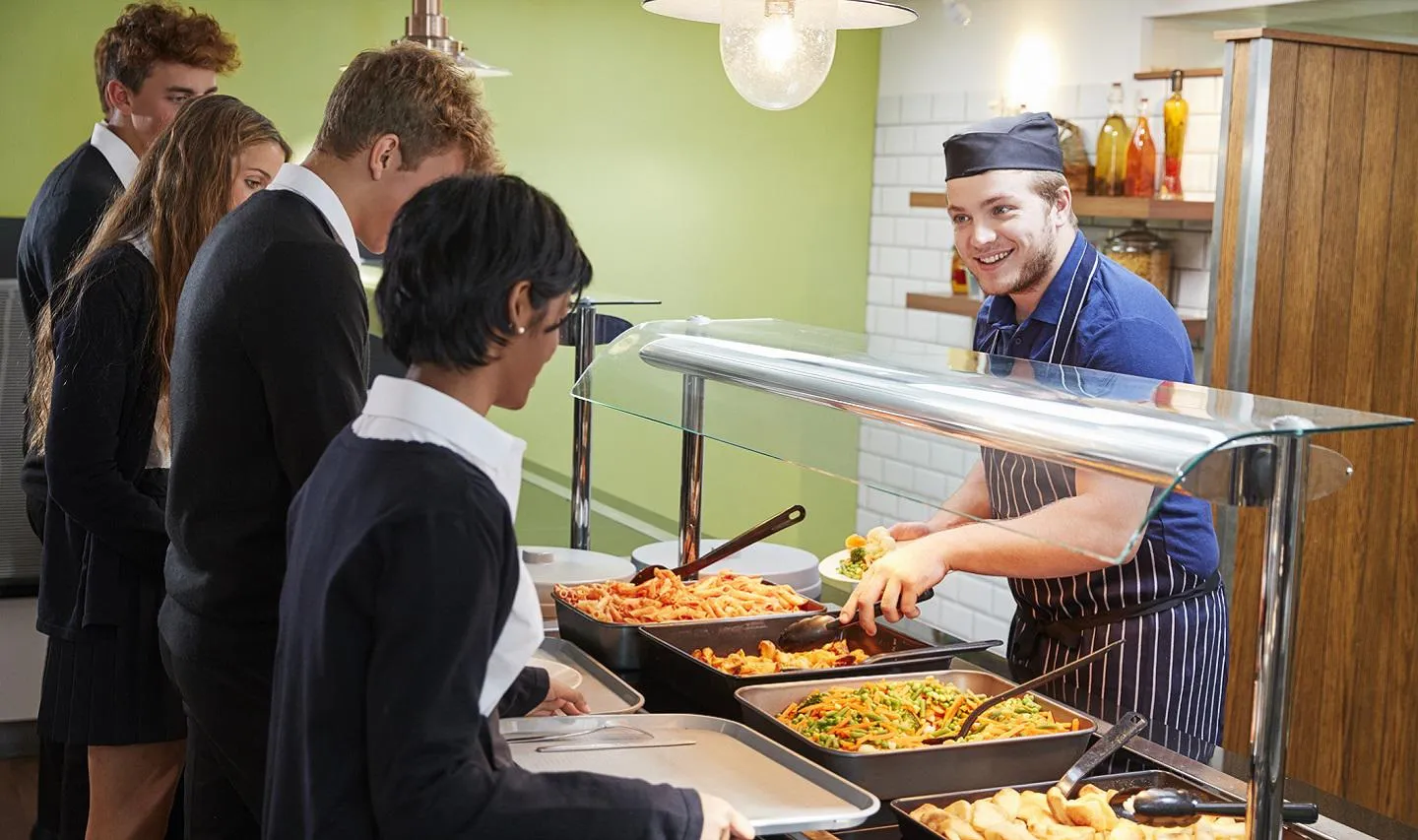 A male canteen staff member serving food to high school students