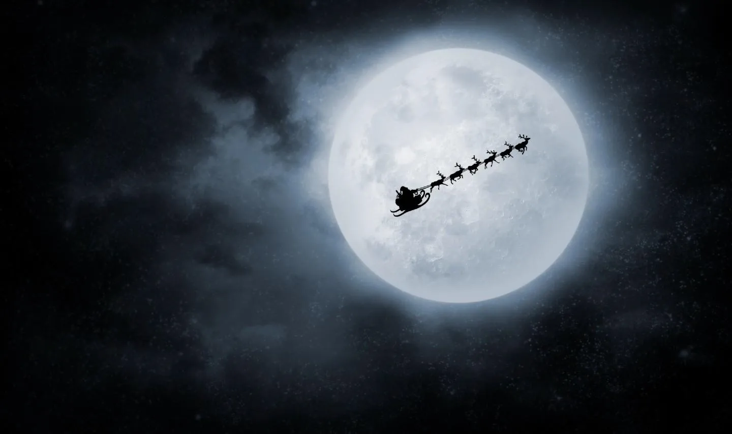 silhouette of santa's sleigh and reindeer travelling across a full moon.