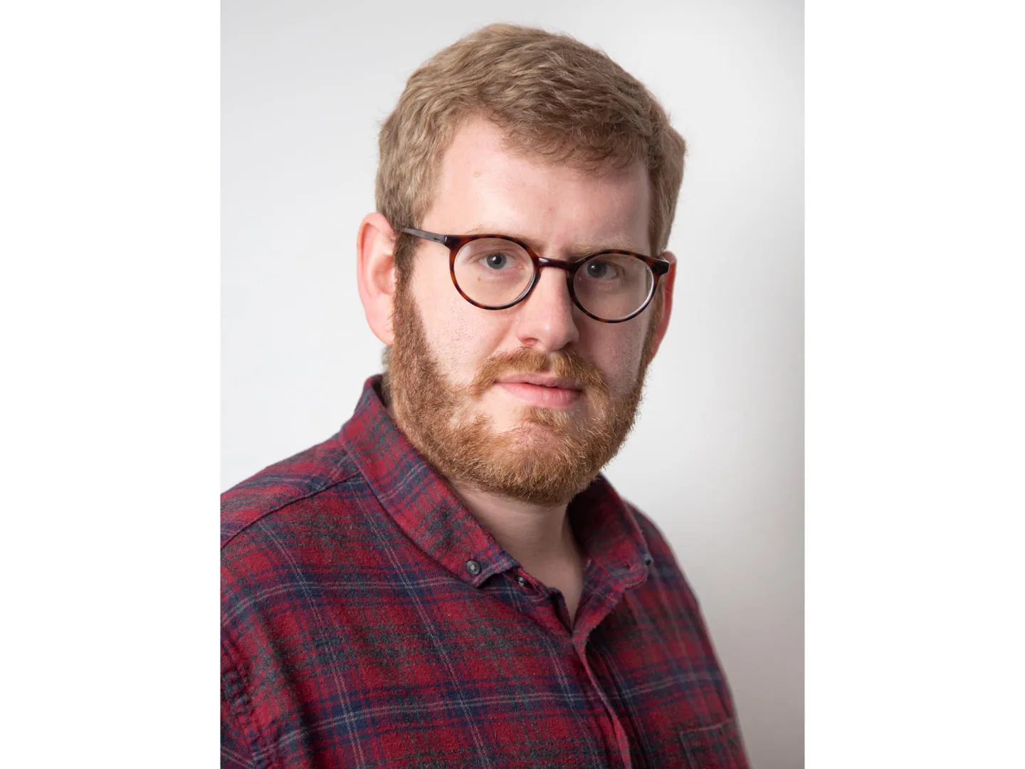 A headshot of Dr Stephen Fielden, a white man with blonde hair and beard, wearing glasses and a red shirt.