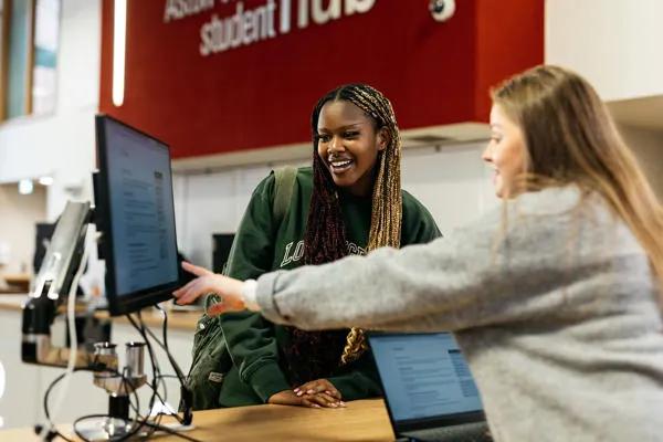 Student being shown something on a computer by a member of staff in the student hub