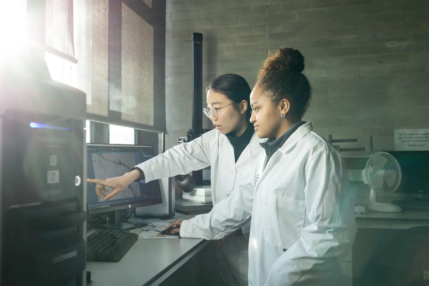 Two women in labcoats pointing at screen