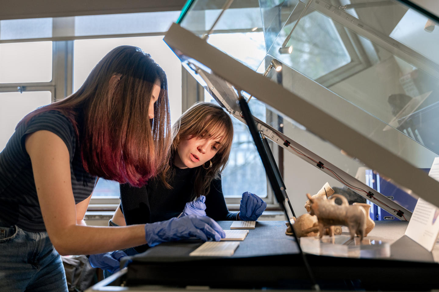 Two women inspecting artefacts in a glass cabinet