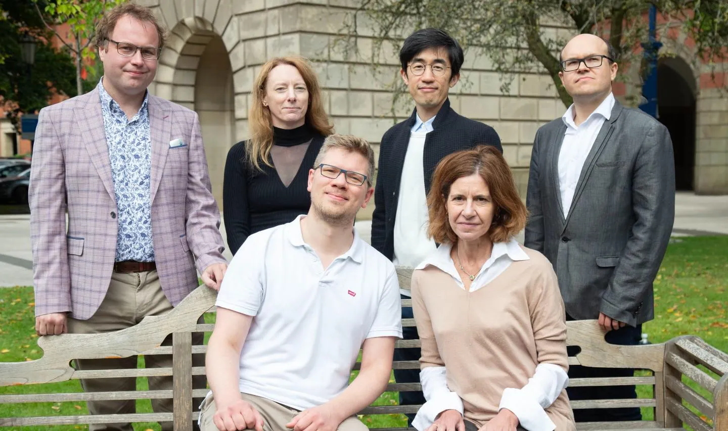 Six academics pictured outdoors by a bench