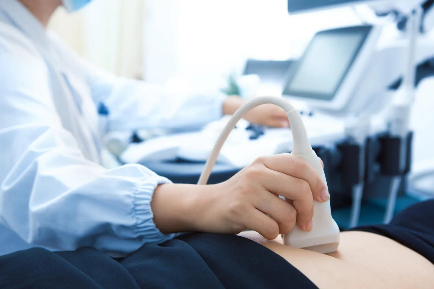 A close up of a sonographers hand using ultrasound scanning on a woman's abdomen 