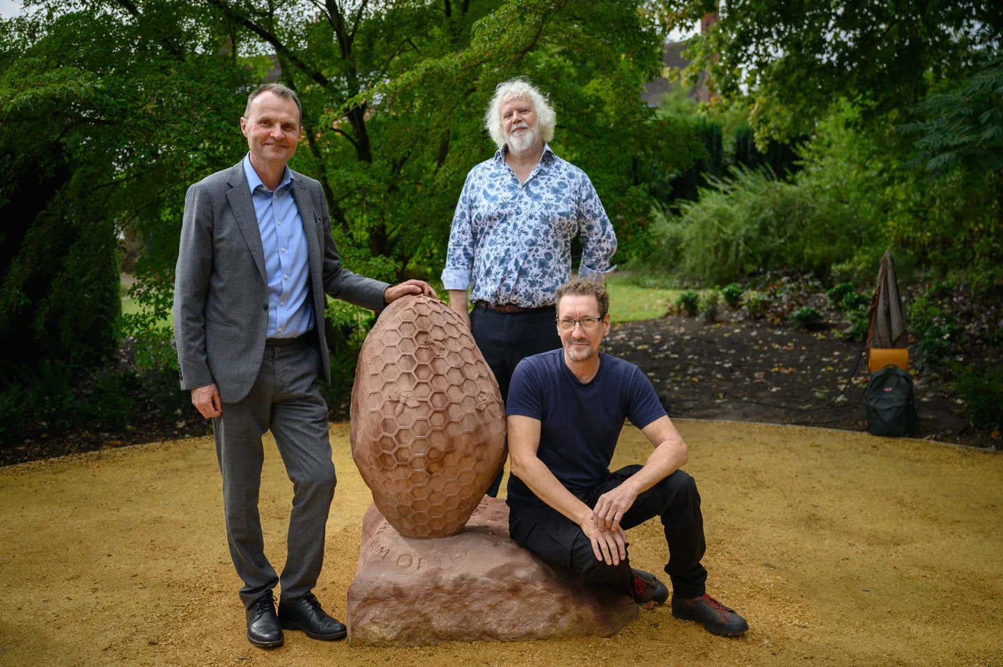 Professor Adam Tickell, Mark Noad and Dan Meek pose next to Dan's stone sculpture of bees and honeycomb