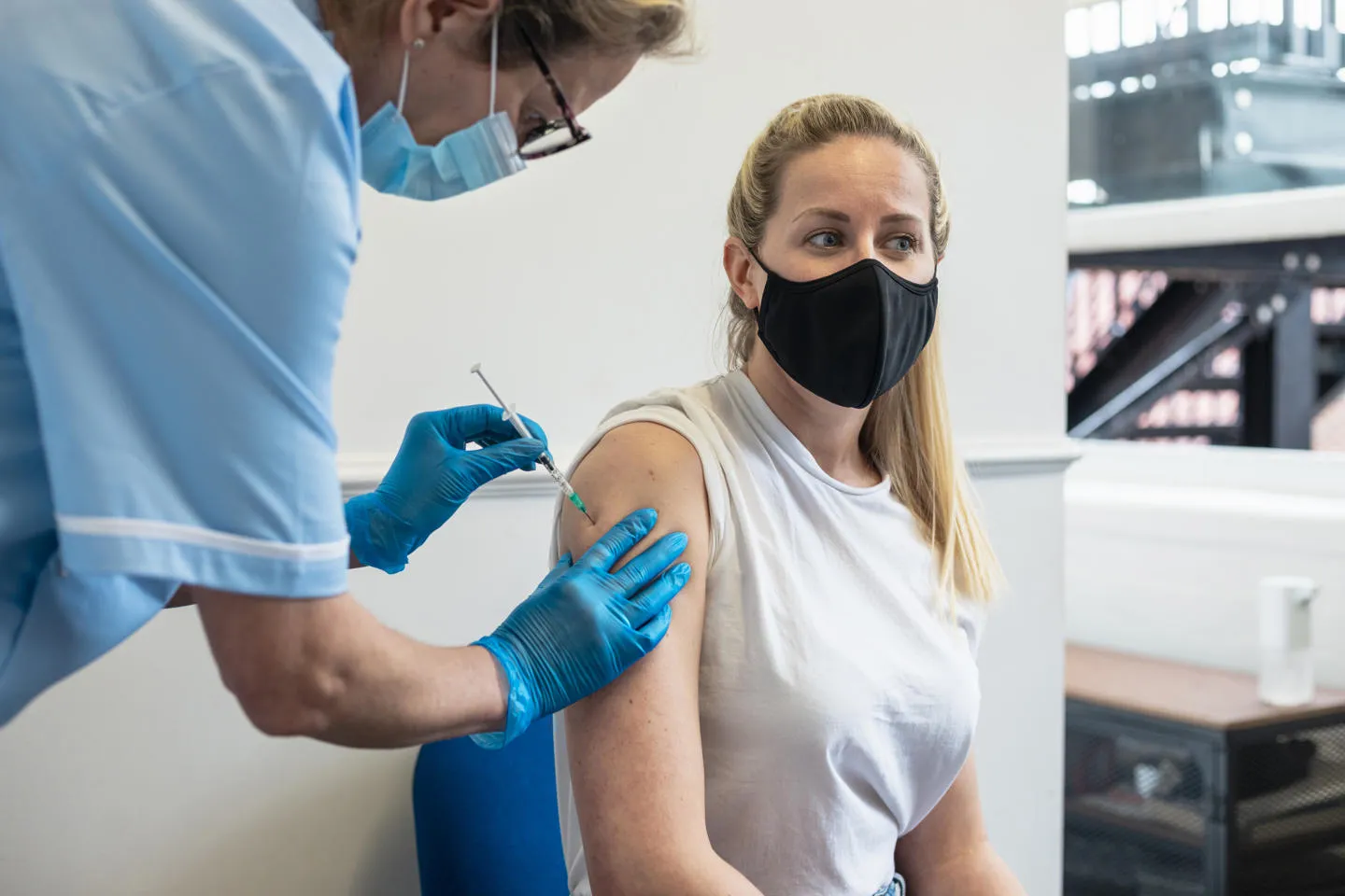 A nurse injecting a masked patient with a vaccine