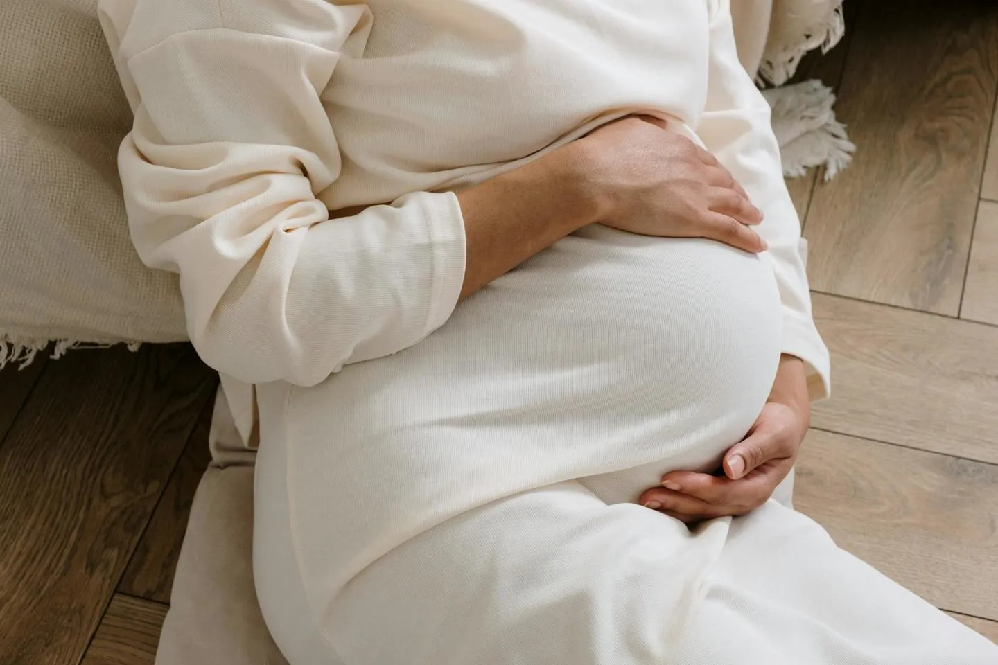 Expectant mum wearing white dress holding her tummy while lying on pillows on floor 