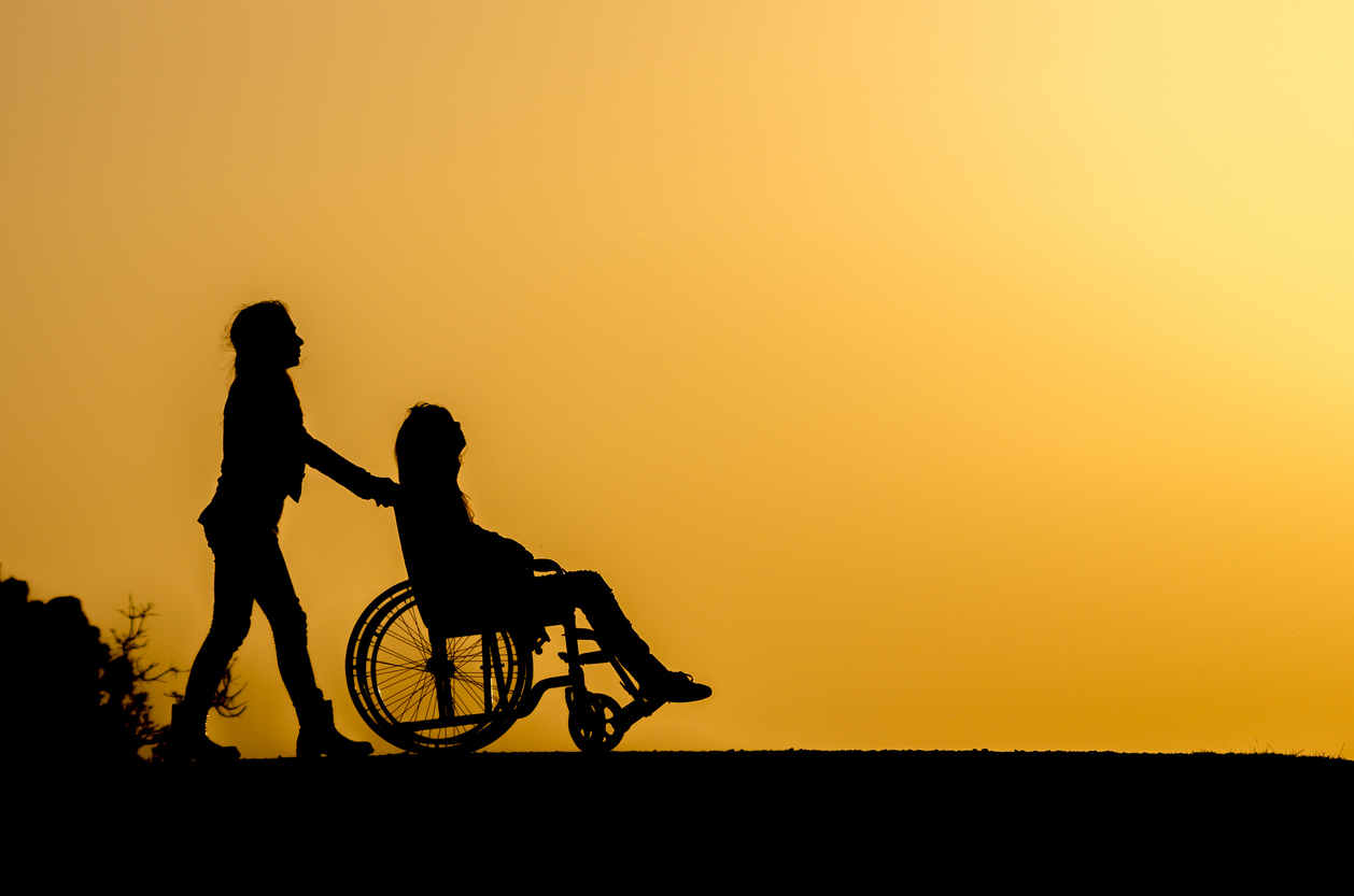 Woman pushing a teenage child in a wheelchair in silhouette.