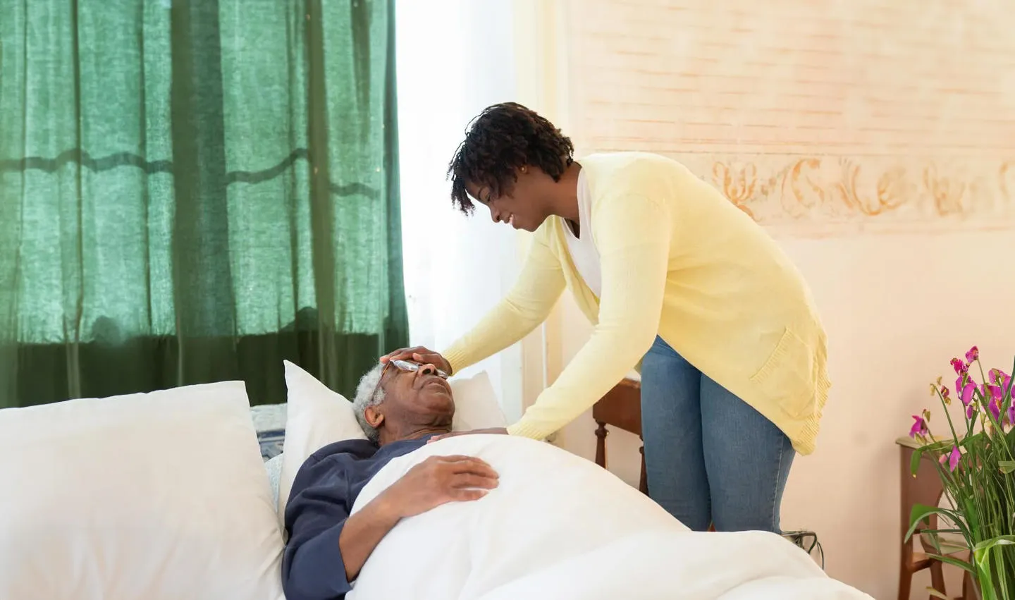 A woman caring for elderly man lying down on a bed